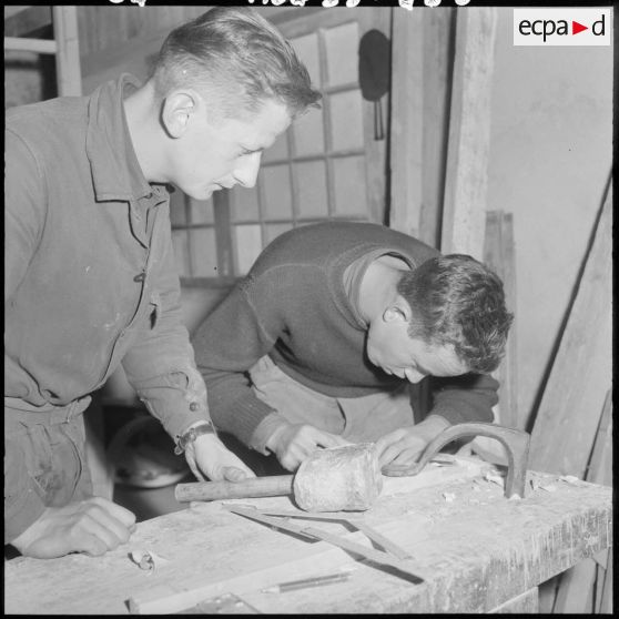 Centre de formation de la jeunesse algérienne : le moniteur de l'atelier de menuiserie, Luchez César, soldat de 2ème classe de la 58/1B, menuisier-ébéniste dans le civil à Lillers (Pas-de-Calais), dirige les premiers travaux d'un élève âgé de 18 ans, de Bou Yamine.