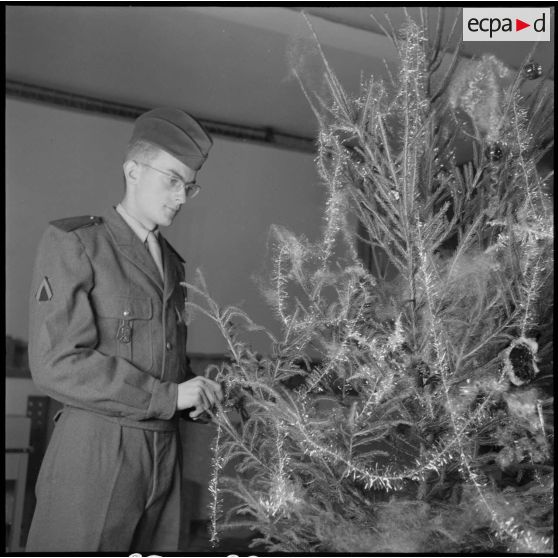 Un soldat décore un arbre de noël.