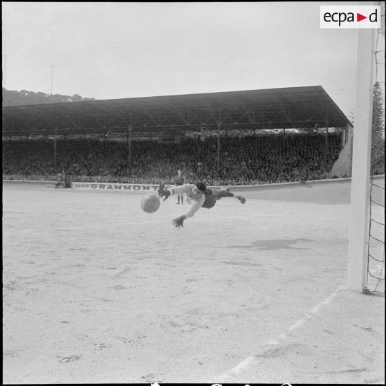 Gardien d’une équipe de football militaire plongeant pour arrêter le ballon en suspension lors d’un match en Algérie. [Description en cours]