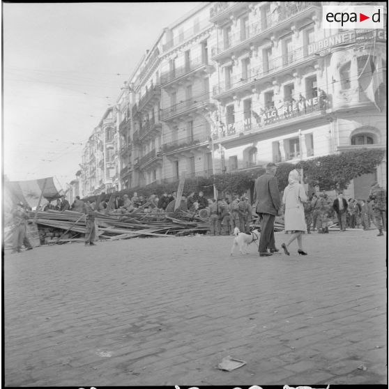 Un couple, passant devant la barricade "Hernandez" et le poste de commandement de Joseph "Jo" Ortiz situé dans la rue Charles Péguy.