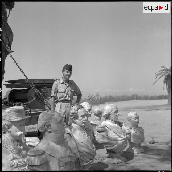 Soldat posant au milieu des bustes sculptés déposés pour le rapatriement en France.