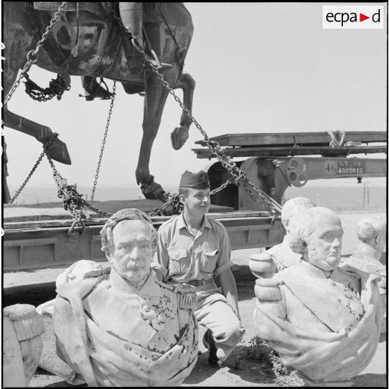 Soldat posant au milieu des bustes sculptés déposés pour le rapatriement en France.