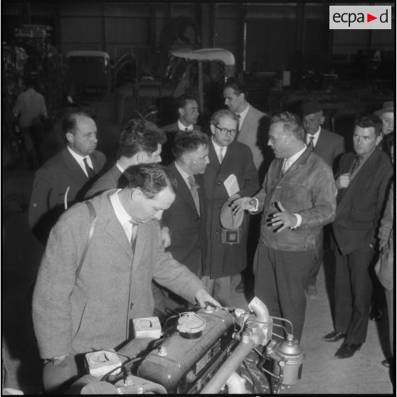M. Barth du Sénat fédéral de l'Allemagne de l'Ouest, est penché sur un moteur, pendant que M. Blaise des services publicitaires donne des renseignements.