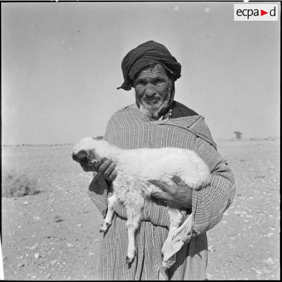 Un berger Reghibat avec un agneau dans ses bras.
