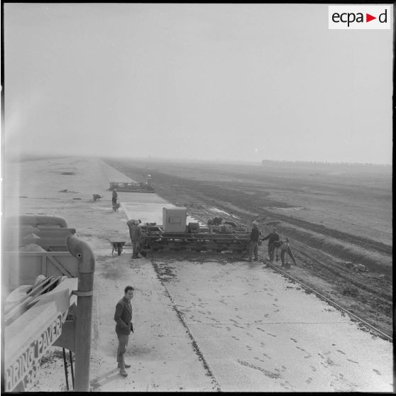 Aérodrome de Maison Blanche. Chantier de la nouvelle piste Est-Ouest en béton précontraint. Le béton une fois déversé, les vibro-lisseuses suivent et aplanissent tout en tassant le béton.