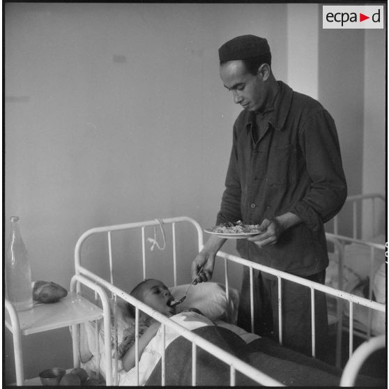 Tlemcen. Hôpital civil. Un homme donne à manger à un enfant.
