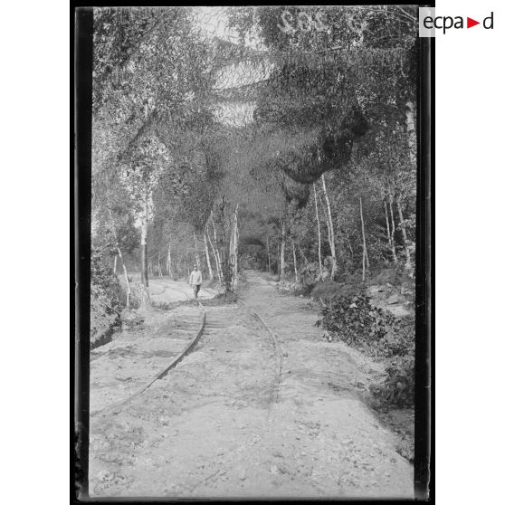 [Un soldat marche le long d'une voie ferrée camouflée.]