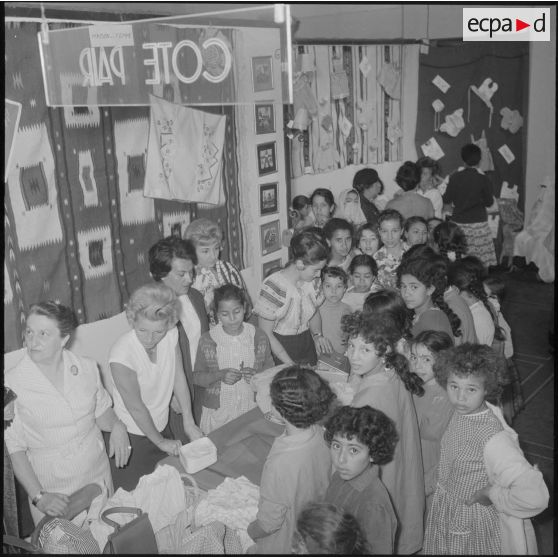 Alger. Salle Pierre Bordes. Vente de la production des cercles de solidarité féminine de l'Algérois. De jeunes filles d'un des Cercles féminins contemplent leurs travaux.