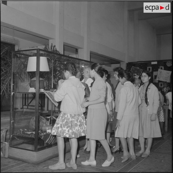 Alger. Salle Pierre Bordes. Vente de la production des cercles de solidarité féminine de l'Algérois. De jeunes filles d'un des Cercles féminins contemplent leurs travaux.