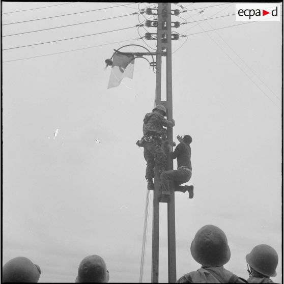 Alger. Belcourt. Un soldat grimpe sur un poteau électrique pour déloger un enfant qui vient d'y accrocher le drapeau du Front de libération national (FLN).