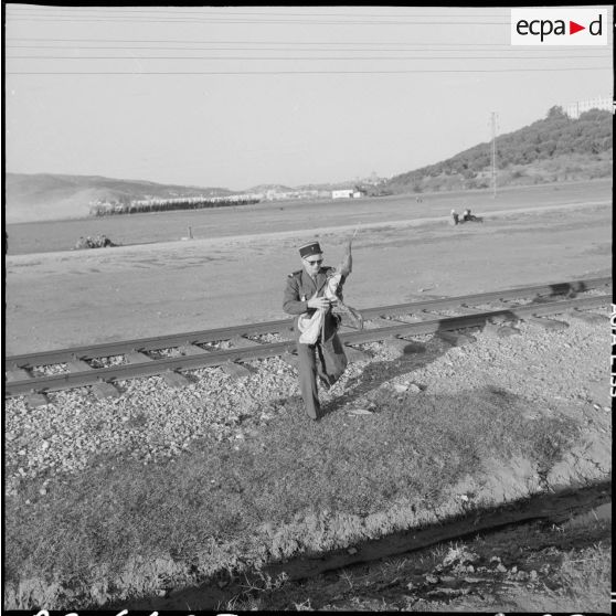 Bône. Manifestations. Un soldat traverse une voie de chemin de fer avec le drapeau du Front de libération national (FLN) dans ses bras.