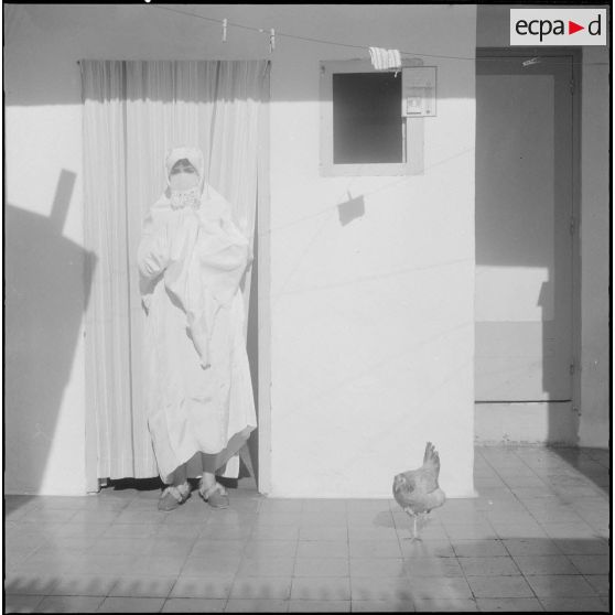 Maison Carrée. Femme posant à l'intérieur de sa maison avec une poule.