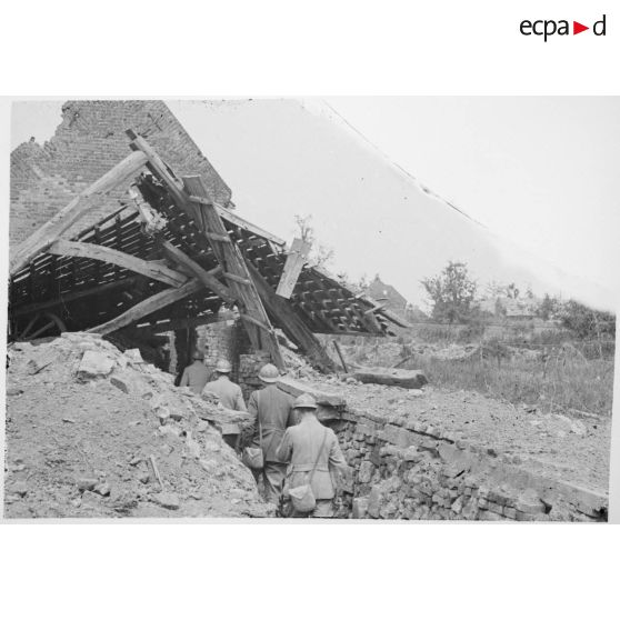 Soldats dans une tranchée devant une maison détruite.