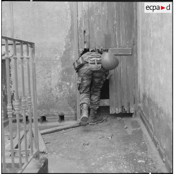 Alger. L'armée boucle le quartier de Bab el Oued. Un soldat parachutiste inspecte derrière une porte en bois cassé.