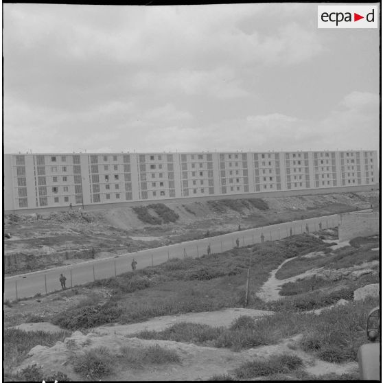 Oran. Fouilles et récupérations d'armes de l'Organisation armée secrète (OAS). Des soldats sont postés le long d'une route face à un immeuble.