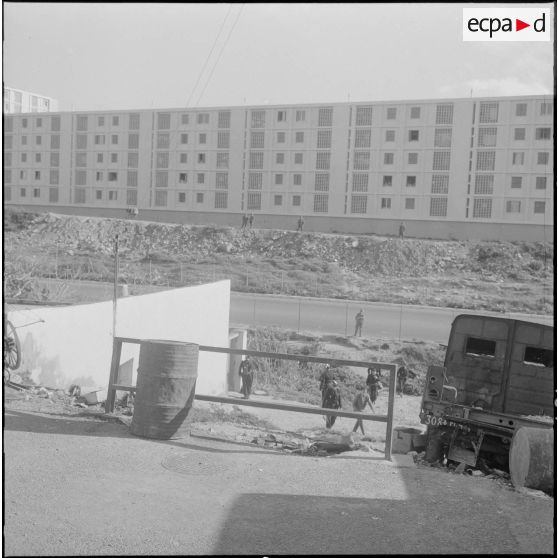 Oran. Fouilles et récupérations d'armes de l'Organisation armée secrète (OAS). Des soldats sont postés le long d'une route face à un immeuble.