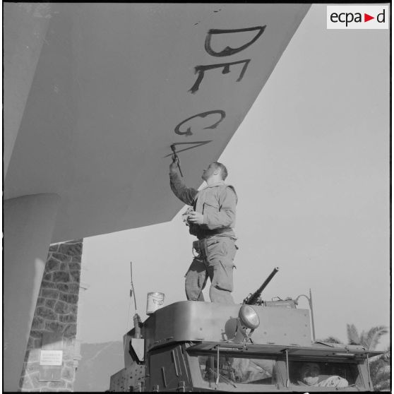Oran. Mise en place des troupes sur les terrasses. Un soldat écrit "Vive De Gaulle" à la peinture, à l'entrée d'un immeuble.