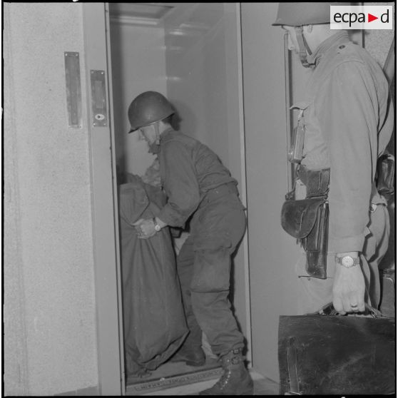 Oran. Mise en place des troupes sur les terrasses. Des soldats chargent des sacs dans un ascenseur.