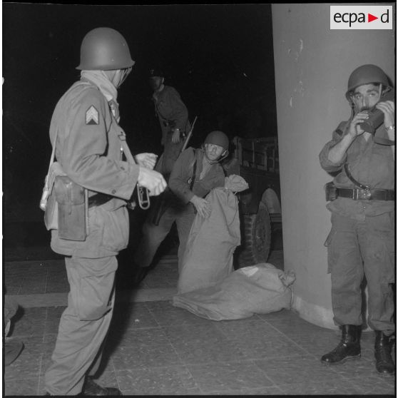 Oran. Mise en place des troupes sur les terrasses. Des soldats sortent des sacs d'un camion, en bas d'un immeuble.