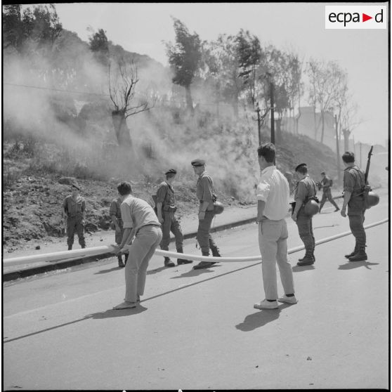 Alger. Quartier des Tagarins. Explosion d'un camion-citerne. Des civils aident les pompiers à installer la lance à incendie, sous le regard des soldats.