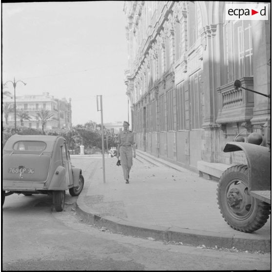 Oran. Suite d'une fusillade place Foch. Un soldat marche au milieu des débris de pierres devant l'hôtel de ville.