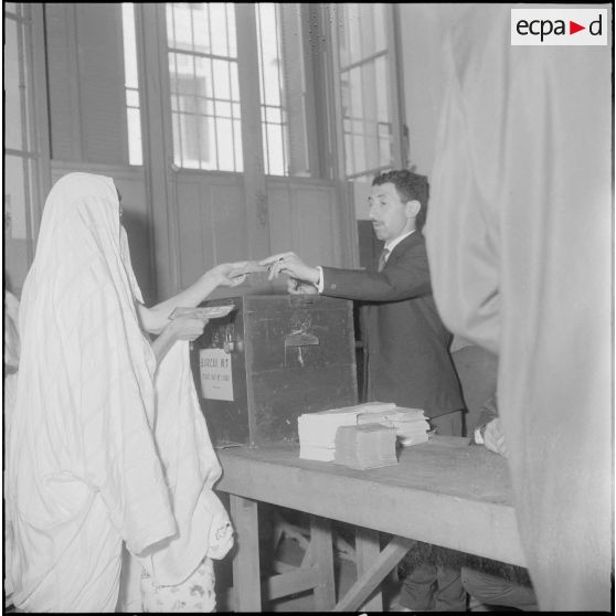 Journée de vote pour le référendum d'autodétermination (1er juillet 1962). Une femme tend ses papiers d'identités à un assesseur au bureau de vote n°1.