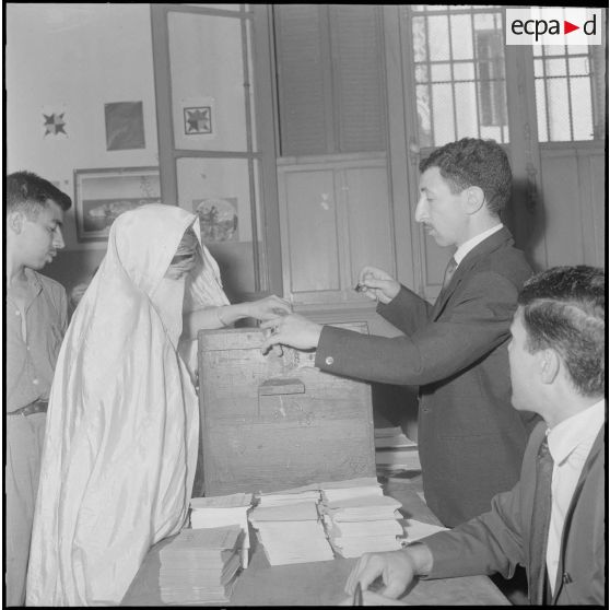 Journée de vote pour le référendum d'autodétermination (1er juillet 1962). Une femme glisse son bulletin de vote dans l'urne face à un assesseur du bureau de vote n°1.