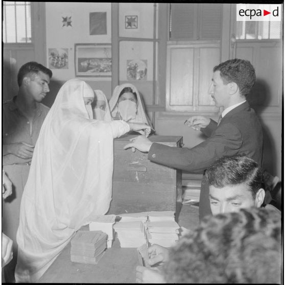 Journée de vote pour le référendum d'autodétermination (1er juillet 1962). Une femme glisse son bulletin de vote dans l'urne face à un assesseur du bureau de vote n°1.