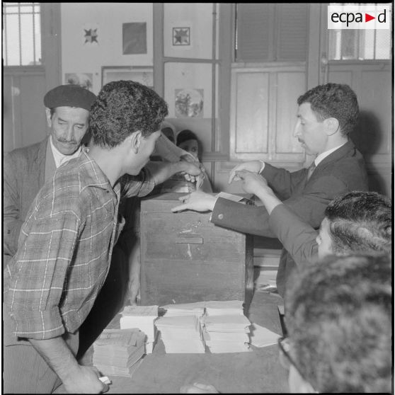 Journée de vote pour le référendum d'autodétermination (1er juillet 1962). Une homme glisse son bulletin de vote dans l'urne face à un assesseur du bureau de vote n°1.
