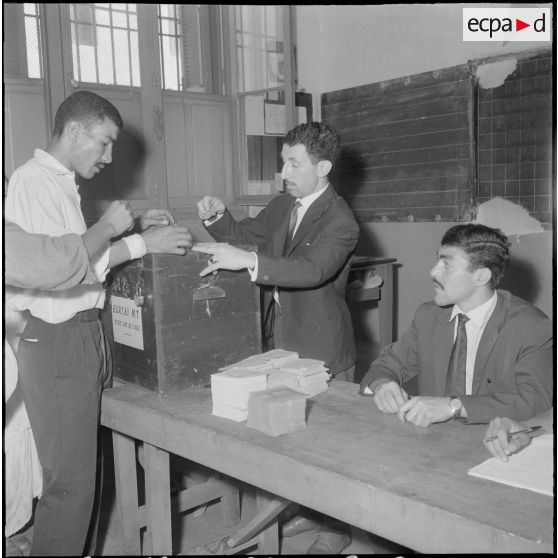 Journée de vote pour le référendum d'autodétermination (1er juillet 1962). Une homme glisse son bulletin de vote dans l'urne face à un assesseur du bureau de vote n°1.