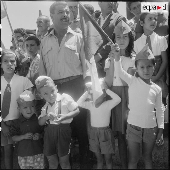 Des enfants parmi la foule brandissant des drapeaux algériens pour la cérémonie de lever des couleurs algériennes.