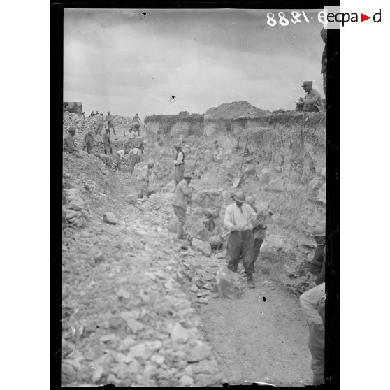 [Des soldats creusent un terrain rocheux, sous le regard d'autorités militaires.]