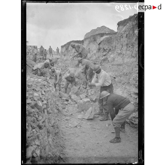[Des soldats creusent un terrain rocheux, sous le regard d'autorités militaires.]