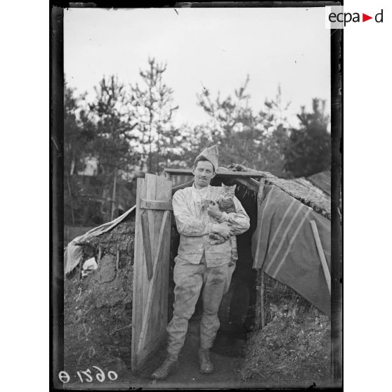 [Portrait d'un soldat qui tient un chat dans ses bras, devant un abri.]