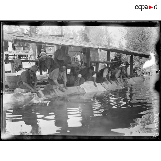 [Vie quotidienne militaire : des soldats lavent leur linge sur le bord d'un lavoir, dans un cantonnement.]