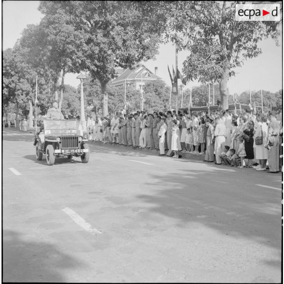 12 L'autorité militaire supérieure remonte l'avenue principale où la foule s'est massée, à bord d'une jeep. [description provisoire]