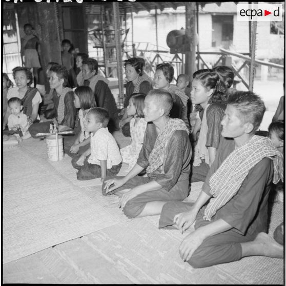 Dans un angle de la salle, des femmes assistent au repas des bonzes. [description provisoire]