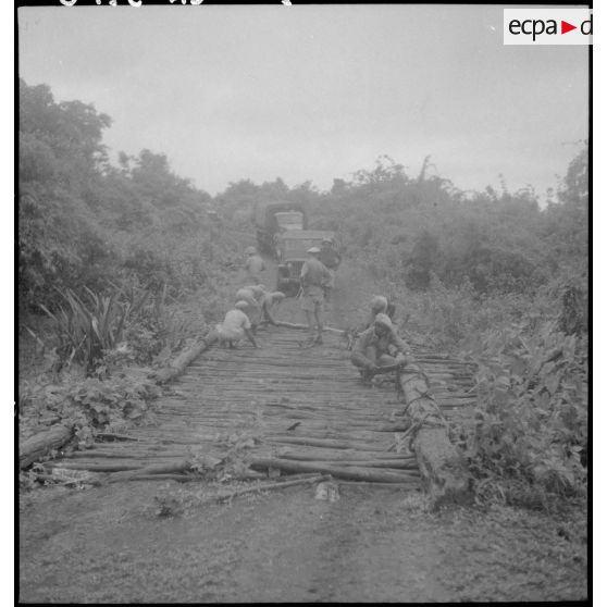 1 à 2 Des militaires aménagent un pont avec des rondins pour permettre le passage d'un convoi de camions GMC 6 X 6. [description provisoire]