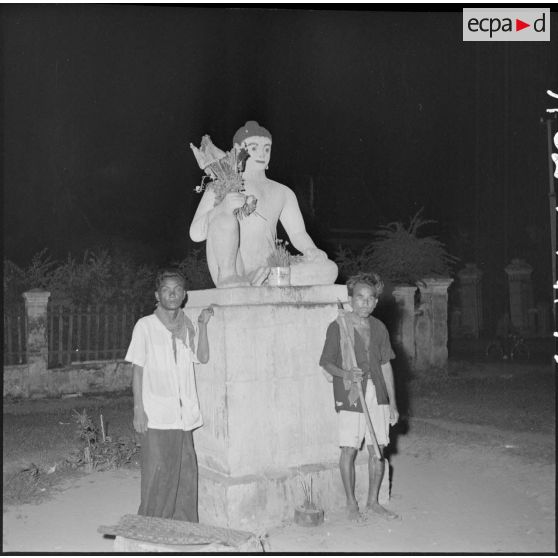 41Deux Cambodgiens debout au pied d'une statue érigée sur un socle. [description provisoire]
