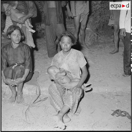 65 Une jeune femme cambodgienne nourrit son bébé, assise sur le bord d'un trottoir. [description provisoire]