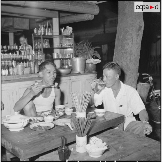 Deux Cambodgiens assis à une table mangent du riz dans une rue de Phnom Penh. [description provisoire]