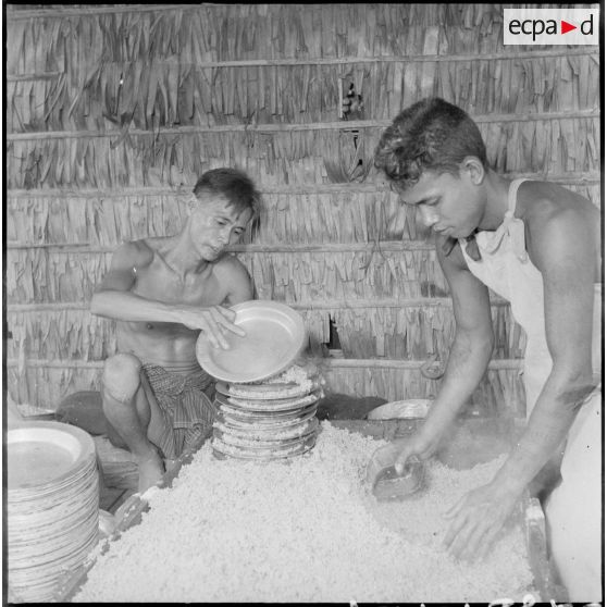 Deux prisonniers du camp de Kompong Cham remplissent des assiettes de riz blanc dans la cuisine. [description provisoire]