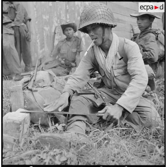 Un caporal du 19e bataillon vietnamien affute son coupe-coupe dans un moment de repos, au cours de l'opération Typhon en plaine des Joncs. [description provisoire]