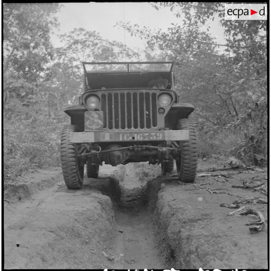 102 Partie avant d'une jeep, vue en contre-plongée roulant sur un chemin creusé en son milieu. [description provisoire]