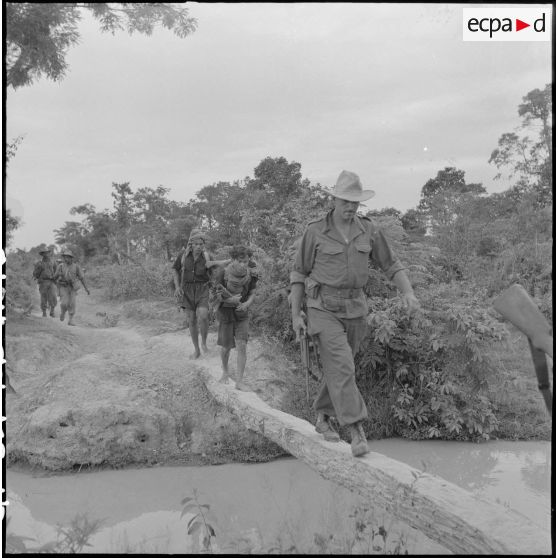 16 Le sous-lieutenant Marty, originaire de Bergerac (Dordogne) traverse une petite rivière sur un pont de fortune. [description provisoire]
