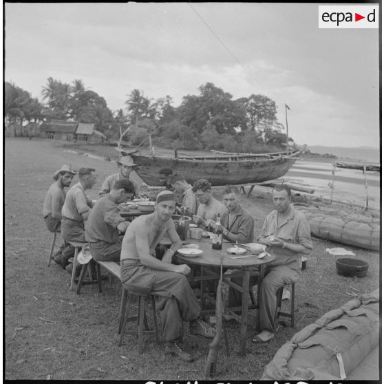 49 Les hommes (probablement du 2/6e RIC) déjeunent à proximité de la plage, à côté de bateaux pneumatiques. [description provisoire]