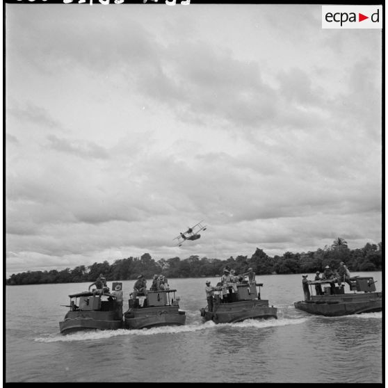 Convoi de vedettes blindées du 4e régiment de dragons survolées par un hydravion sur la rivière de Saigon.