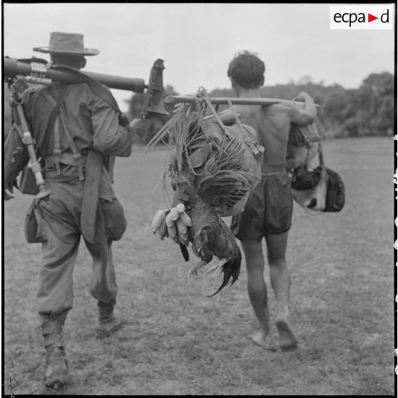 Un chasseur du 3e BCC (Bataillon de Chasseurs Cambodgiens) portant un mortier de 60 mm, accompagné d'un coolie (porteur) lors de l'opération ""Sirocco"". [description provisoire]