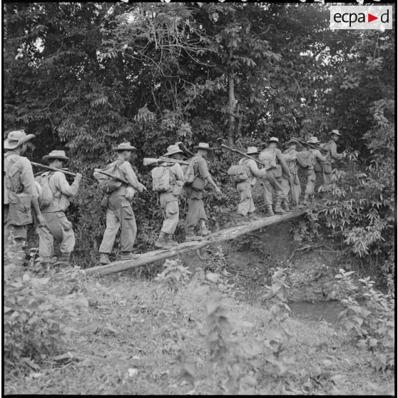 Une section du 3e BCC (Bataillon de Chasseurs Cambodgiens) traverse un petit cours d'eau sur un pont de fortune, lors de l'opération ""Sirocco"". [description provisoire]