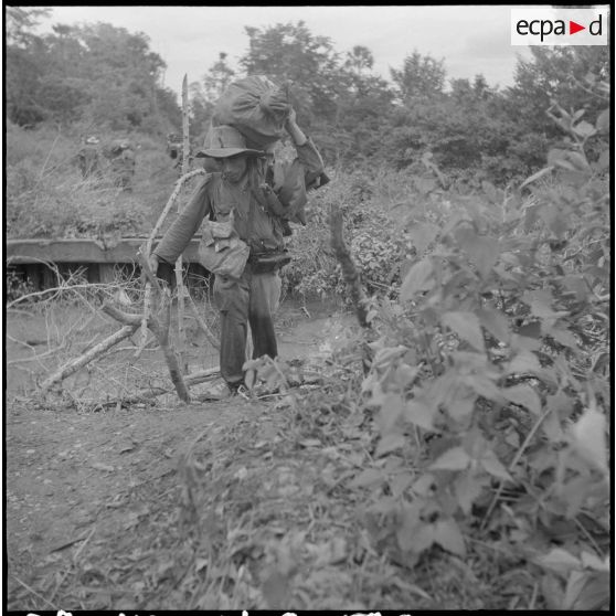 Un tirailleur du 3/4e RTT (3e bataillon du 4e Régiment de Tirailleurs Tunisiens) passe un ""ponts de singe"", lourdement chargé de son paquetage. Le convoi de relève du poste d'Amléang est confronté à de nombreuses coupures et à un terrain chaotique, ce qui obligent parfois à décharger les camions pour les alléger et  favoriser un franchissement délicat. [description provisoire]